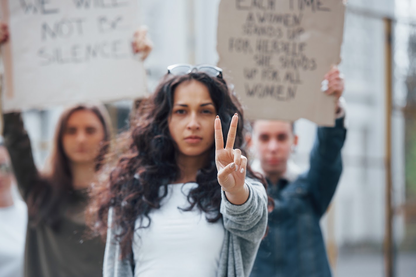 Group of people protesting, with a focus on a the peace sign being used by the women in the front